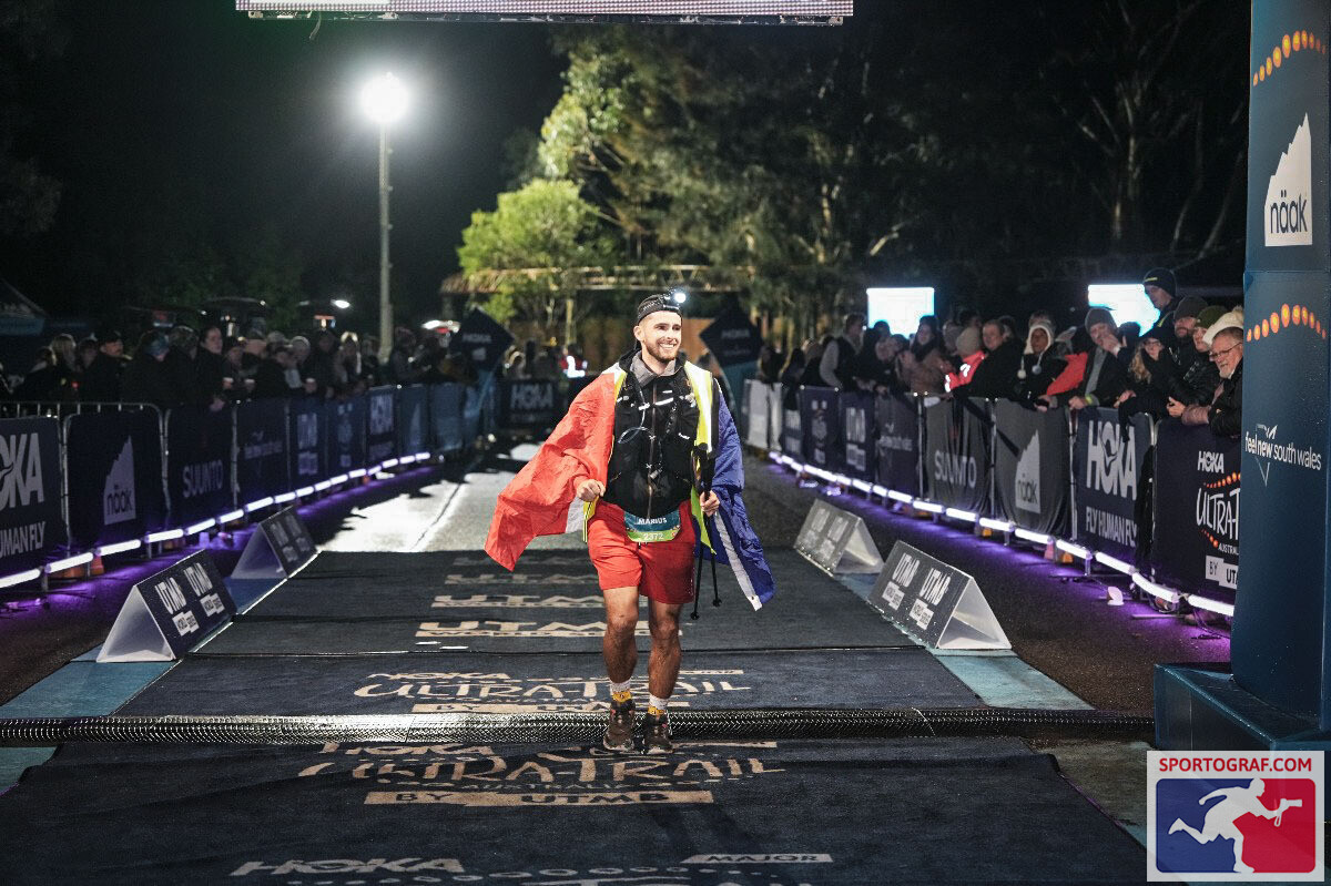 Marius franchissant la ligne d'arrivée de l'Ultra-Trail Australia, drapeau français sur les épaules