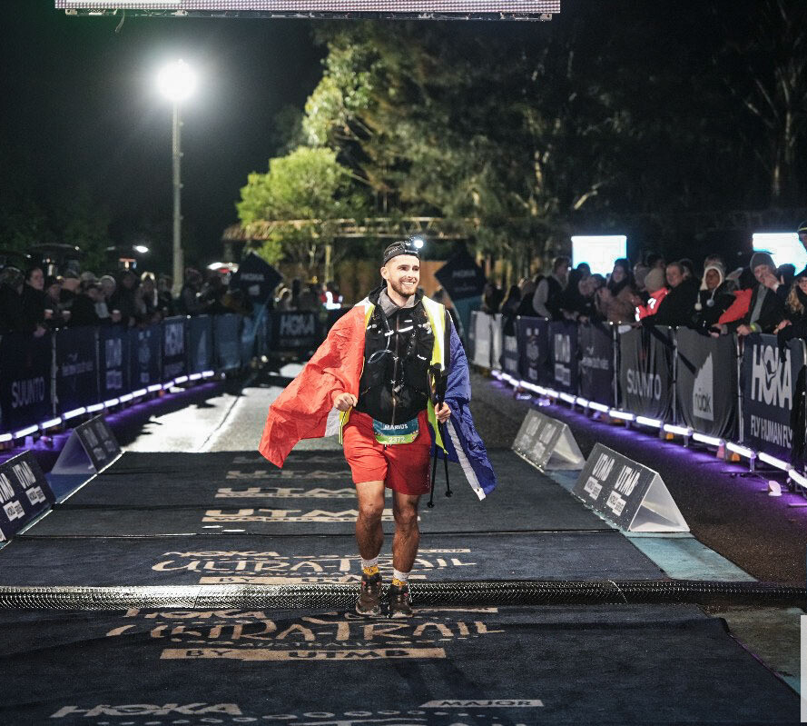 Marius franchissant la ligne d'arrivée de l'Ultra-Trail Australia, drapeau français sur les épaules